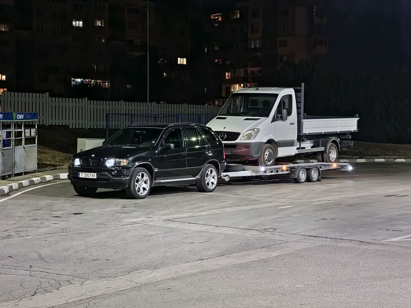 BMW X5 towing a Mercedes Sprinter at night